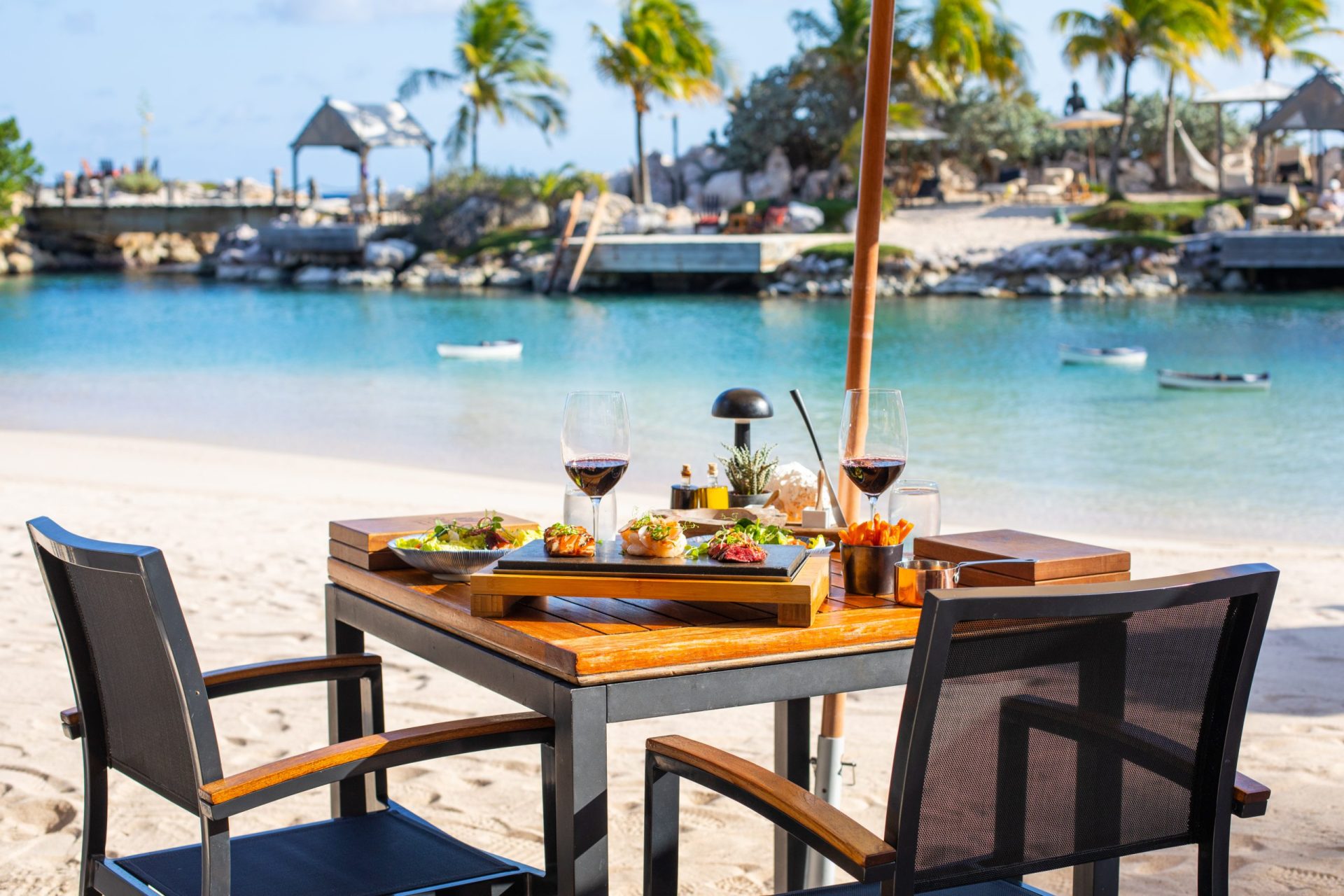 Table with food and wine on it on the beach with water in the background